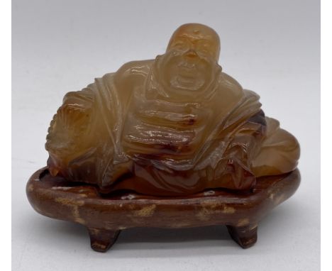 A carved hardstone figure of Buddha (possibly jade) on wooden stand, width 9.5cm