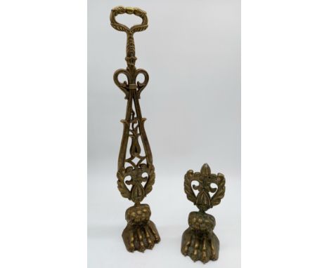A vintage brass doorstop with pierced decoration on a lion paw, and another similar but smaller.