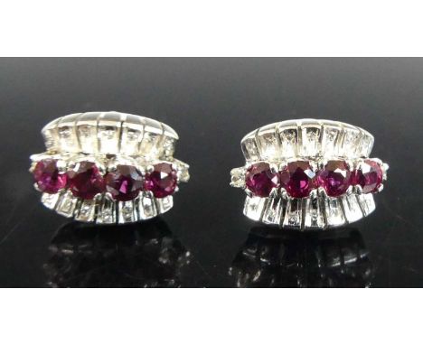 A pair of white metal ruby and diamond half-hoop earrings, each with four round cut rubies within a border of 16 single and r