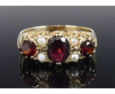 A yellow metal, garnet and pearl half-hoop ring, having three graduated garnets and four 2mm seed pearls in scalloped claw se