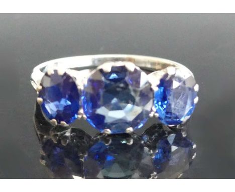 A white metal sapphire three stone ring comprising a centre round and two oval cut sapphires in claw settings. Centre sapphir