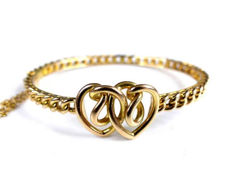 An Edwardian 15ct gold hinged bangle, centred with two intertwined hearts, with safety chain, 14.3g, dia.6cm
