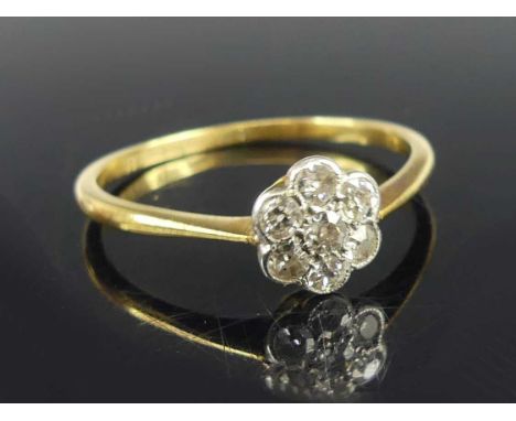 A yellow and white metal diamond circular cluster ring, having seven single cut diamonds in grain and bezel settings, diamond