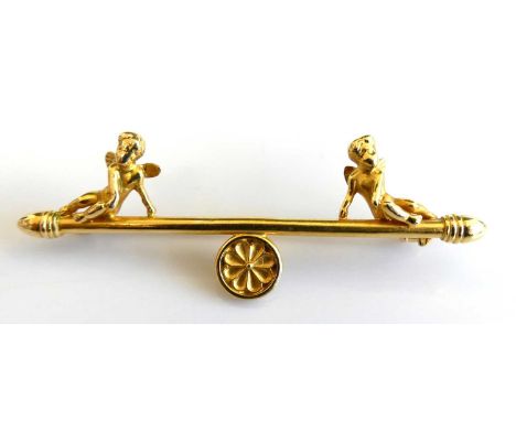 A yellow metal bar brooch with 2 cherubs seated on a finial surmounting a circular floral motif with a safety clip. Brooch le