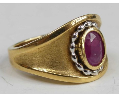 An 18ct gold ruby set heavy dress ring, featuring an oval faceted ruby within a yellow and white beaded bezel setting, ruby d