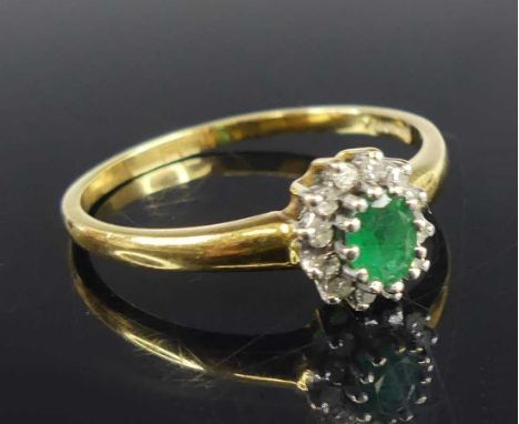 An 18ct yellow and white gold, emerald and diamond oval cluster ring, featuring a centre emerald within a border of twelve si