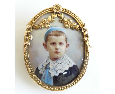 An Edwardian yellow metal miniature portrait brooch, depicting a little boy within a beadwork mount with floral garland detai