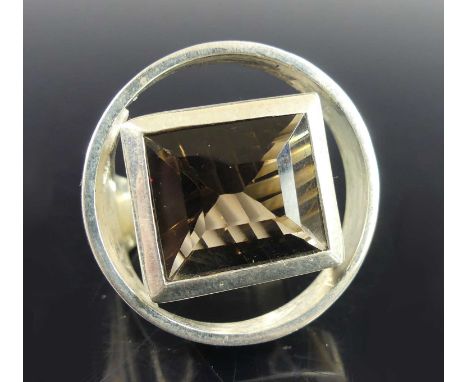 A contemporary silver and smoky quartz set dress ring, the emerald cut quartz bezel set and measuring approx 13.2 x 15.8 x 7.