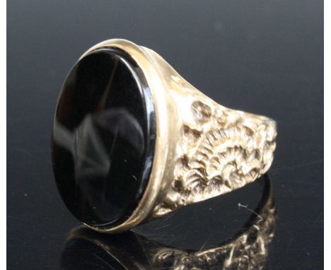 A 9ct yellow gold oval onyx signet ring. The onyx measuring 19.7 by 14.45mm approx. Within a bezel setting with textured shou