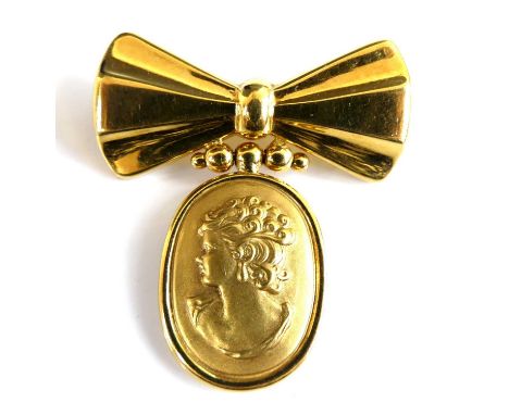 A yellow metal bow shaped bar brooch, having an oval pendant suspended below depicting the bust of a classical woman, with ro