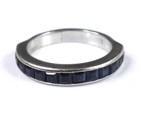 A contemporary white metal and sapphire set half-hoop ring, channel set with 13 princess cut sapphires, size M, stamped 750 a