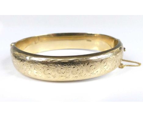 A Victorian style 9ct gold hinged bangle, with safety chain, one side having leaf and flower scroll engraved decoration, Ches