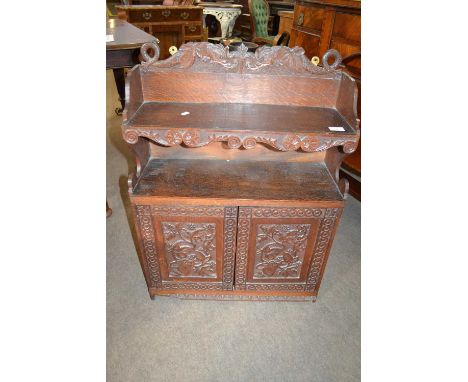 A Victorian Gothic Revival oak wall shelf, cornice decorated with carved sea monsters over a single shelf and two panelled do