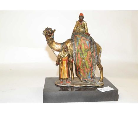 A Bergmann style painted bronze of a Middle Eastern carpet seller astride a camel on black rectangular base, 18cm long