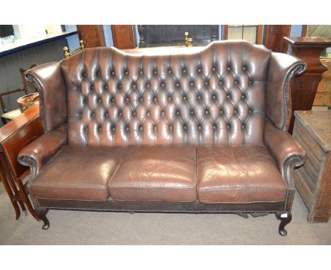 A brown leather Chesterfield style buttoned wing back three seater sofa raised on short front cabriole legs, 178cm wide