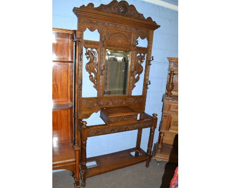 A Victorian Gothic carved oak hall stand with central mirrored panel, sunburst, Green Man and griffin detail, turned front le