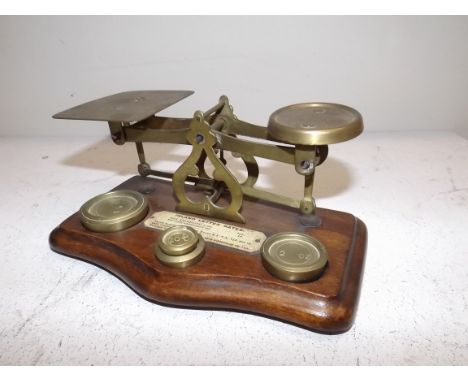 A brass postal scales with wood base, a plaque reads inland letter rate not exceeding 2oz 1 1/2d.