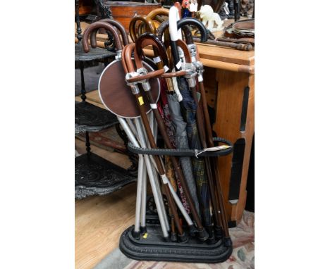 A black cast iron stick stand, having cast iron tray with seven umbrellas and seven assorted shooting sticks (15)