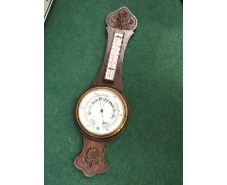An early 20th century oak cased wall barometer and thermometer with carved floral decoration.