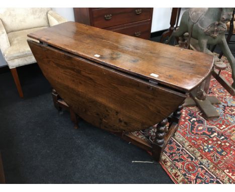 A 4' antique oak gate-leg table resting on barley twist supports, cross stretchers and single drawer.