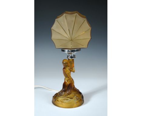 An Art Deco amber glass figural table lamp, modelled as a female nude kneeling on a rocky base, she holds the chrome fitting 