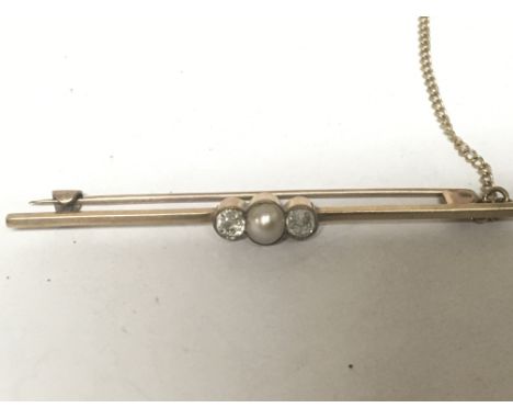 A gold bar brooch set with a central pearl flanked by two old cut diamonds.