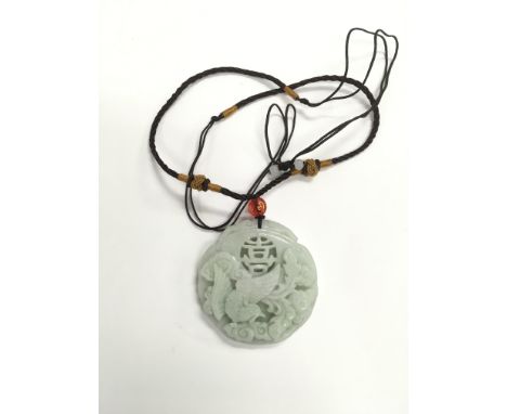 A jade style pendant suspended on a braided cord,