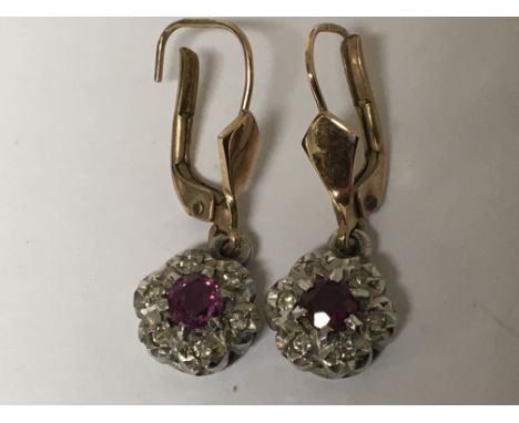 A pair of gold earrings set with a ruby flanked by diamonds.
