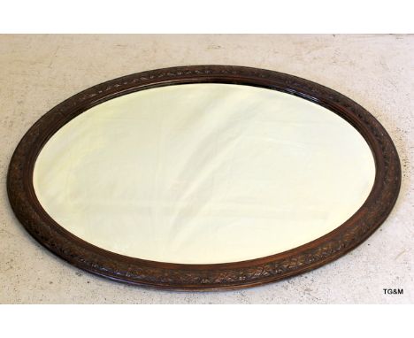 An oval mirror with carved wood surround & bevelled glass