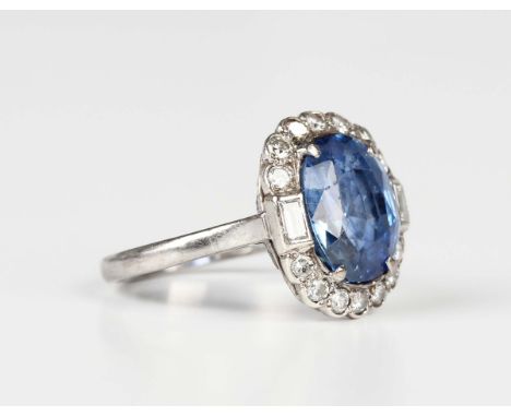 A white gold, sapphire and diamond oval cluster ring, claw set with the oval cut sapphire within a surround of circular cut d