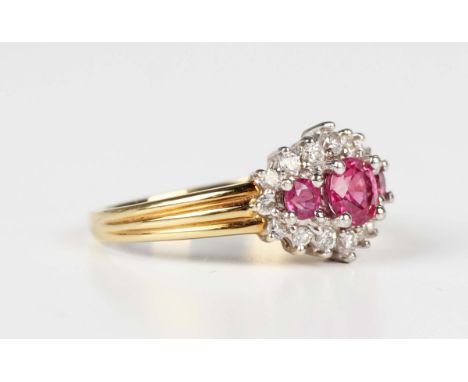 An 18ct gold, ruby and diamond ring, claw set with a row of three circular cut rubies within a surround of circular cut diamo