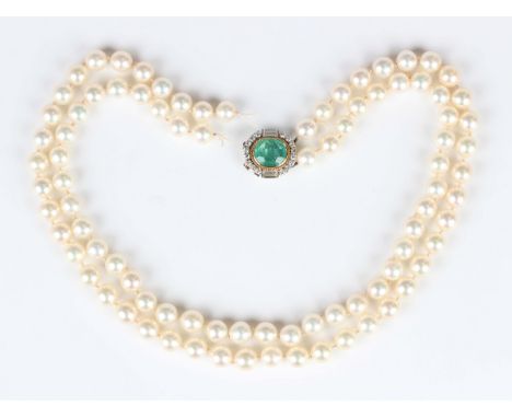 A two row necklace of uniform cultured pearls on a French white gold, emerald and diamond oval clasp, collet set with an oval