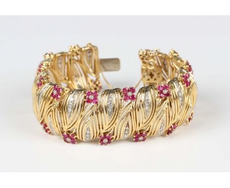 A gold, ruby and diamond bracelet in a stylized wirework foliate design, mounted with circular cut rubies to the flowerheads,