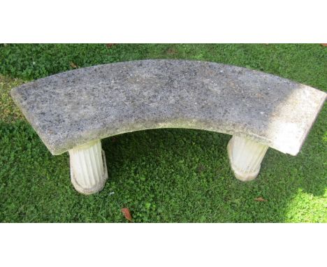 A weathered three sectional cast composition stone garden bench with crescent shaped slab seat, raised on fluted supports, 12