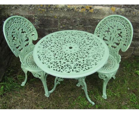 A light green painted cast aluminium garden terrace table with decorative pierced circular top, raised on swept and scrolled 