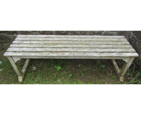 A weathered teak garden bench with rectangular open slatted seat, raised on square cut supports and sledge feet, 140cm long x