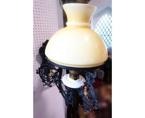 A cast iron wall bracket oil lamp, with a scrolled hinged arm with gold putti detail, shade diam 30cm, and a heraldic machine