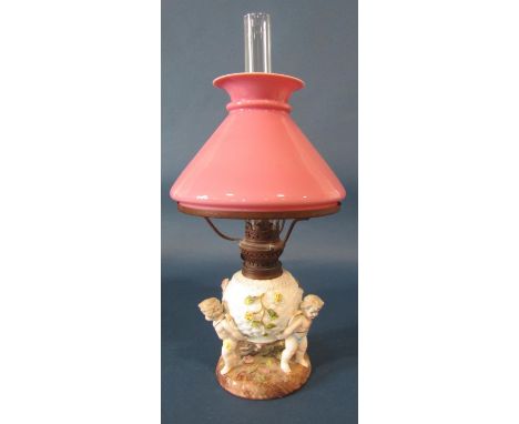 A 19th century German porcelain oil lamp, the lattice work floral encrusted reservoir supported by three cherubs with brass m