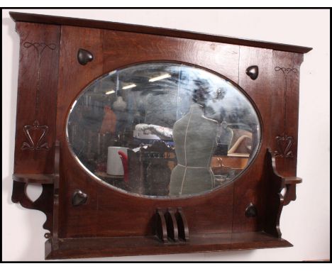 A Victorian oak Arts & Crafts overmantel mirror with shaped bevelled plate mirror having shelf base with embellished panel wo