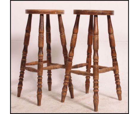 A pair of vintage bar stools having circular saddle seats being raised on turned legs with peripheral foot stretchers. Measur