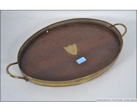 An early 20th century brass and oak butlers tray with pierced brass gallery surround and central armorial cartouche to centre