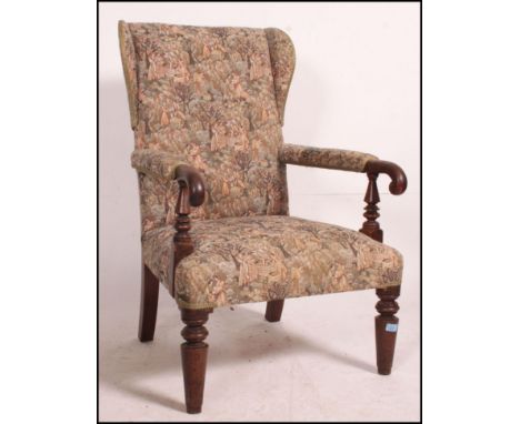 An early 20th century country oak and tapestry upholstered wingback armchair being raised on tapered legs with shaped show wo