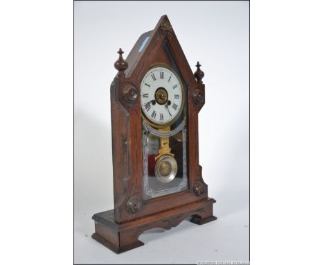 An early 20th century gingerbread American mantel spire clock with glass pendulum window under dial with roman numeral chapte