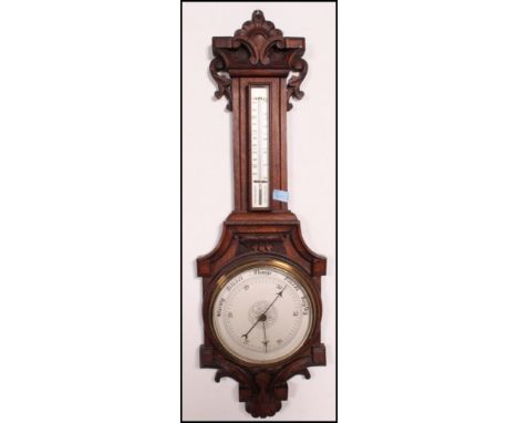 An Edwardian carved oak clock - banjo barometer being carved with foliate decoration, clock above a thermometer in the neck h