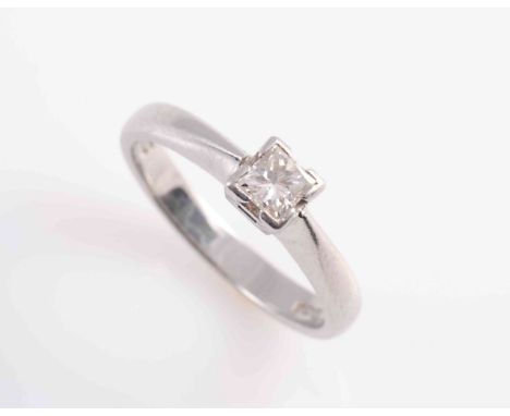 A DIAMOND RING, the square cut diamond four claw set in a simple pierced mount between solid tapering shoulders on a plain ba