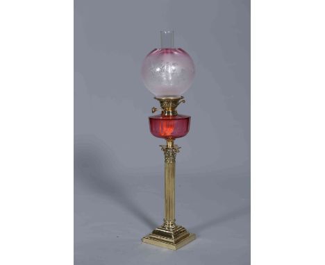 A VICTORIAN BRASS AND CRANBERRY GLASS OIL LAMP, with Corinthian column and stepped square base, the faceted circular reservoi