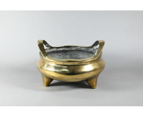 A large 19th century Chinese bronze tripod censer, compressed globular form with loop handles standing on three conical feet,
