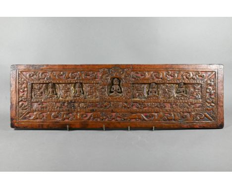 A rectangular hardwood gilded and lacquered panel carved with Buddhist deities in the style of a 16th century Tibetan manuscr