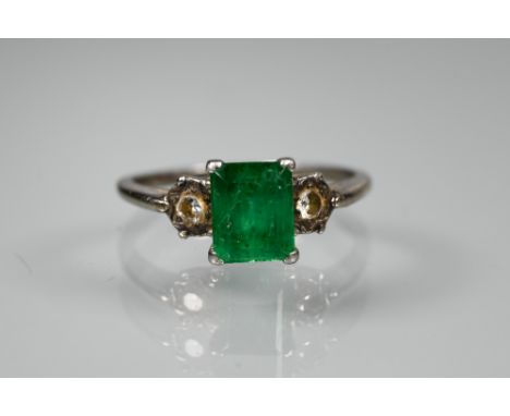 An emerald and diamond ring, the central rectangular emerald with small diamond to each side, unmarked white metal set, size 