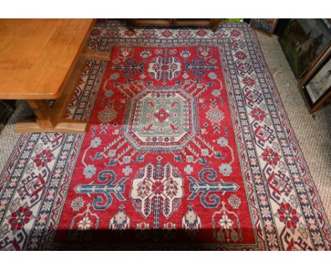 A contemporary Kazak carpet with pale red ground and stylized floral design within camel ground borders, 325 x 228 cm, simila